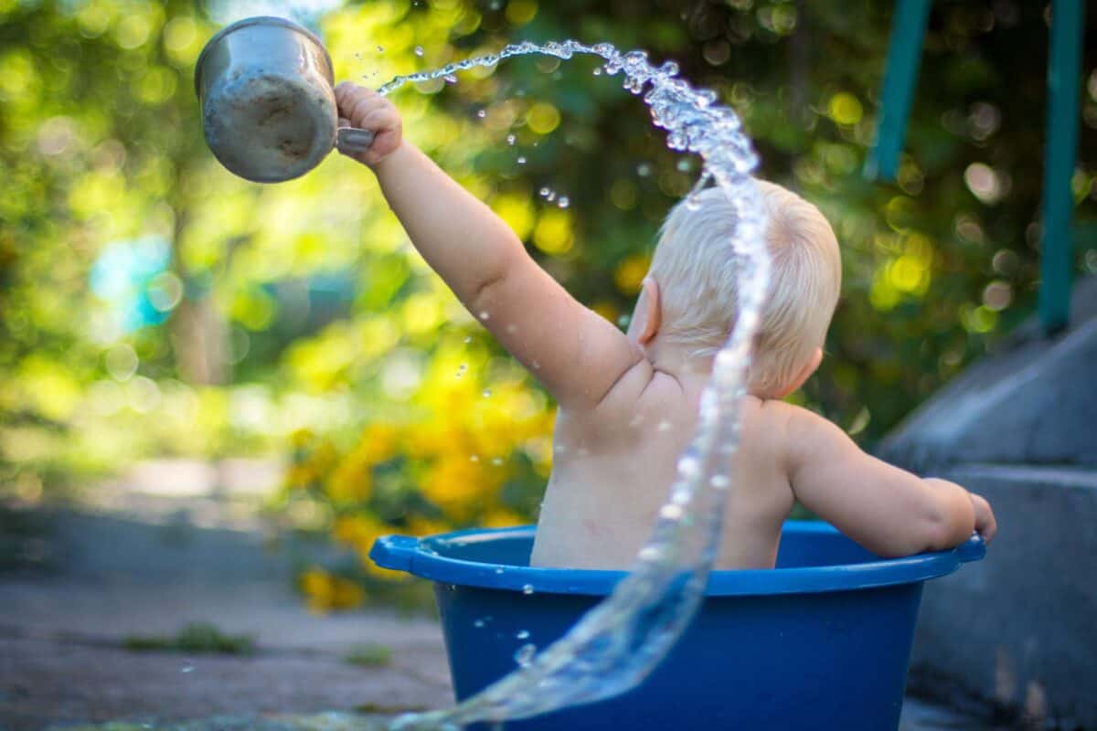 toddler sitting in bucket spilling water 