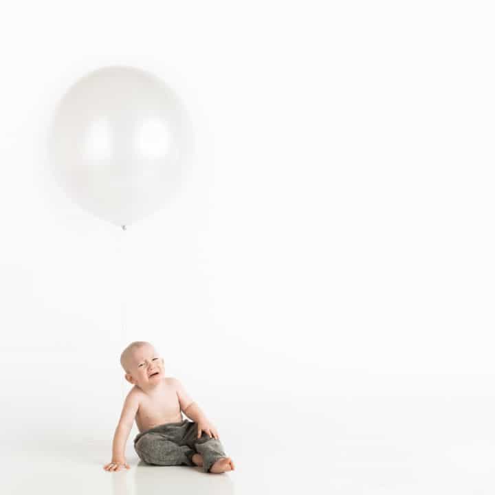 Crying constipated baby sitting underneath a balloon