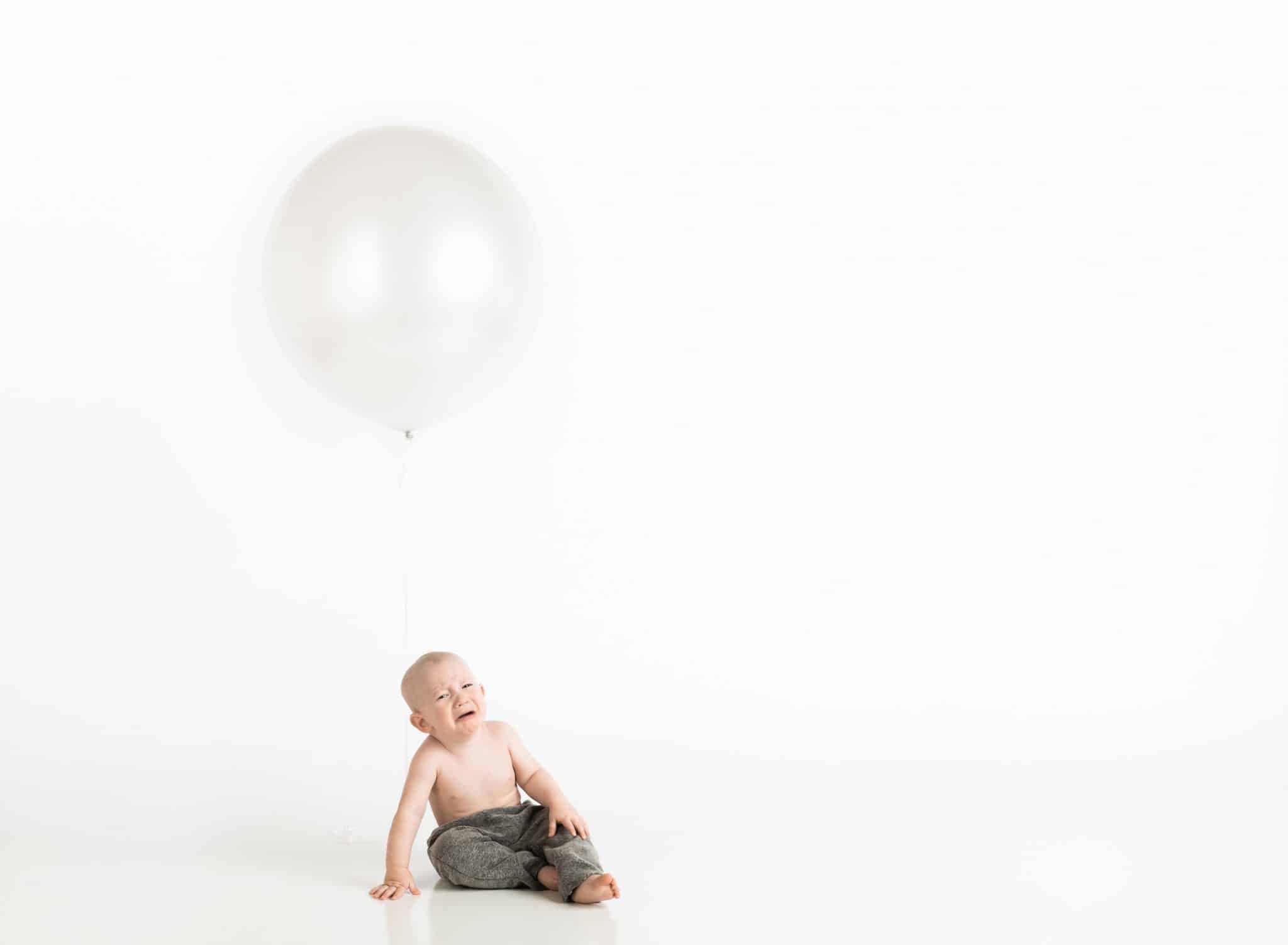 Crying constipated baby sitting underneath a balloon