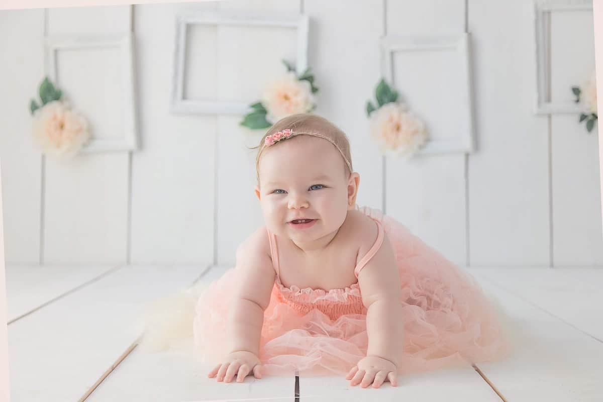 smiling baby in pink dress crawling on floor