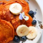 Close up of pumpkin pancakes topped with banana, blueberries and flowers.