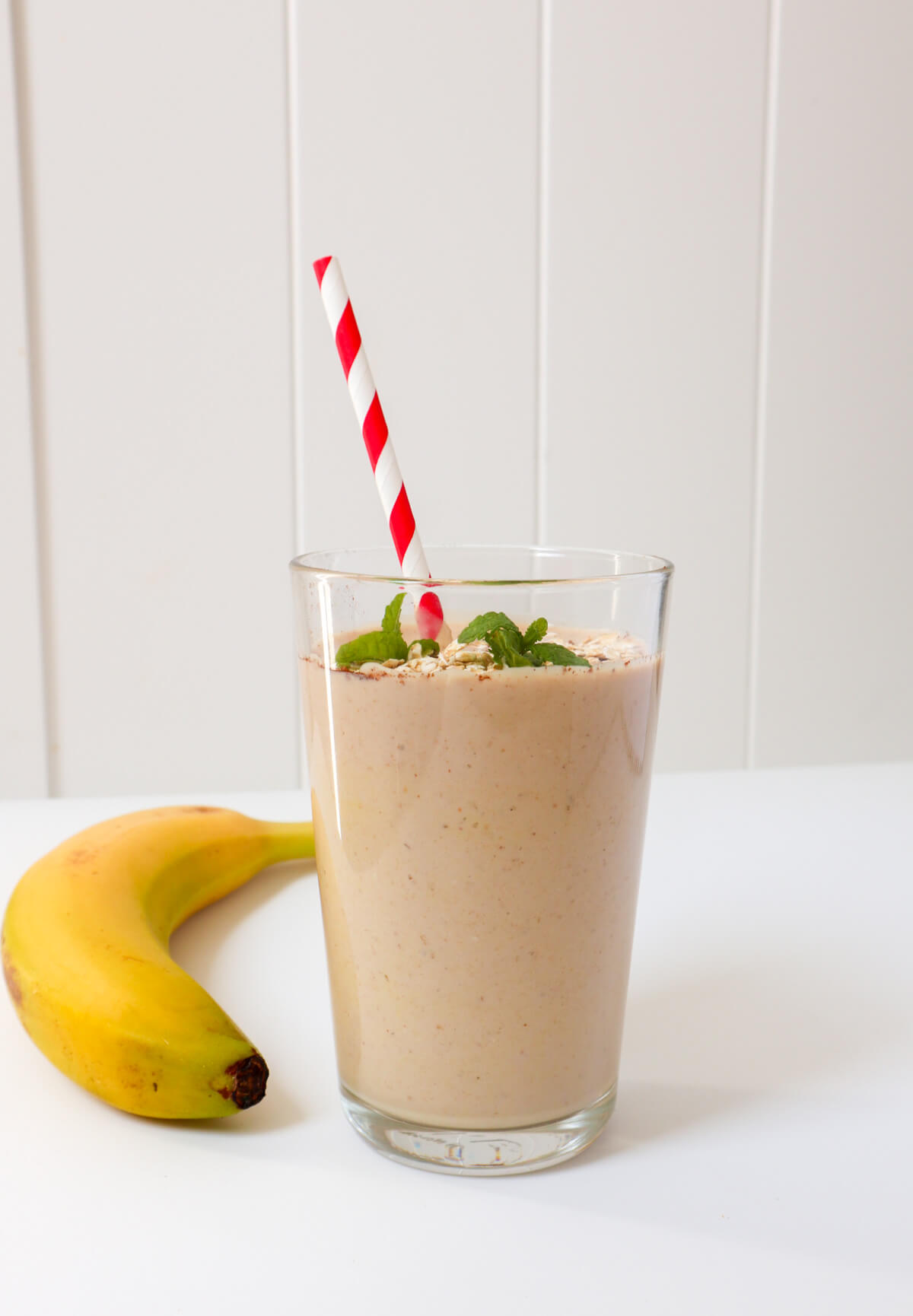 Banana peanut butter oat milk smoothie in a glass on a white background with a red straw in it