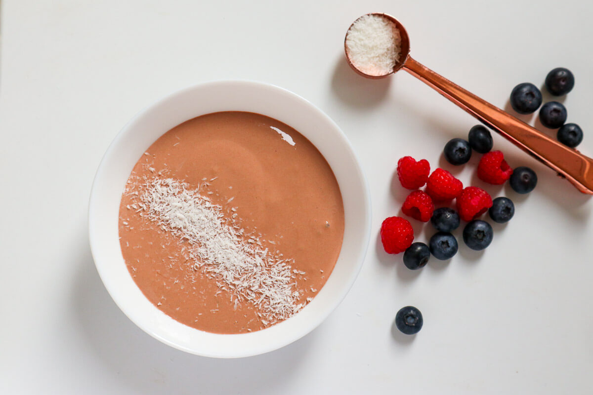 Homemade chocolate yogurt with coconut on top and berries on the side.