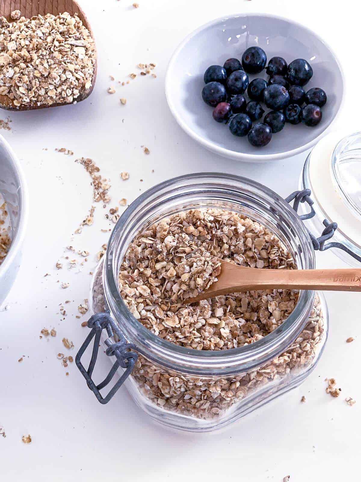 healthy granola in a glass jar with wooden spoon and blueberries on the side
