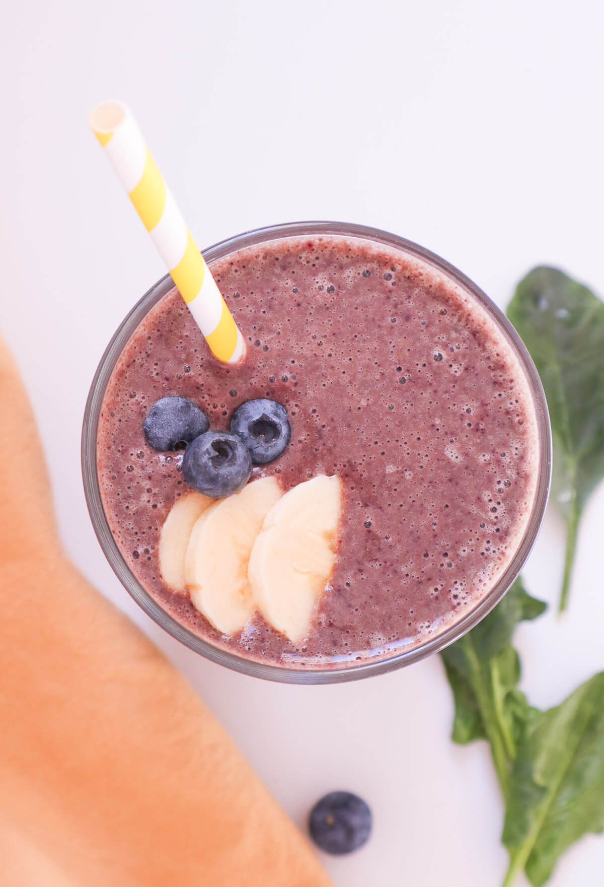 Top down view of purple smoothie with blueberries, bananas and a yellow straw. 
