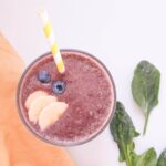 Top down view of purple smoothie with blueberries, bananas and a yellow straw.