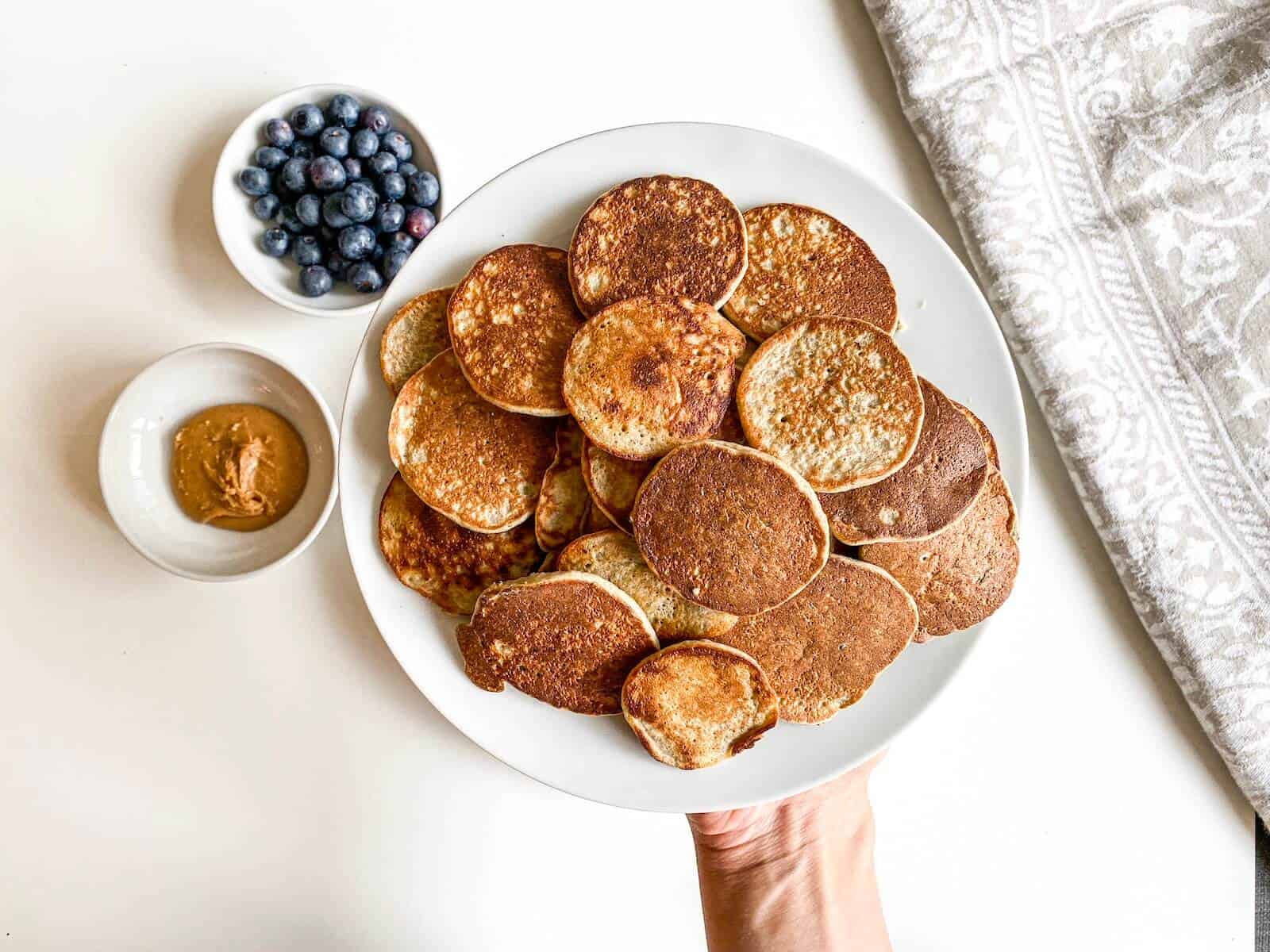 banana chia pancakes held on a plate with peanut butter and blueberries on the side 