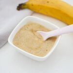 Banana puree for baby with a spoon dipped in and a banana in the background