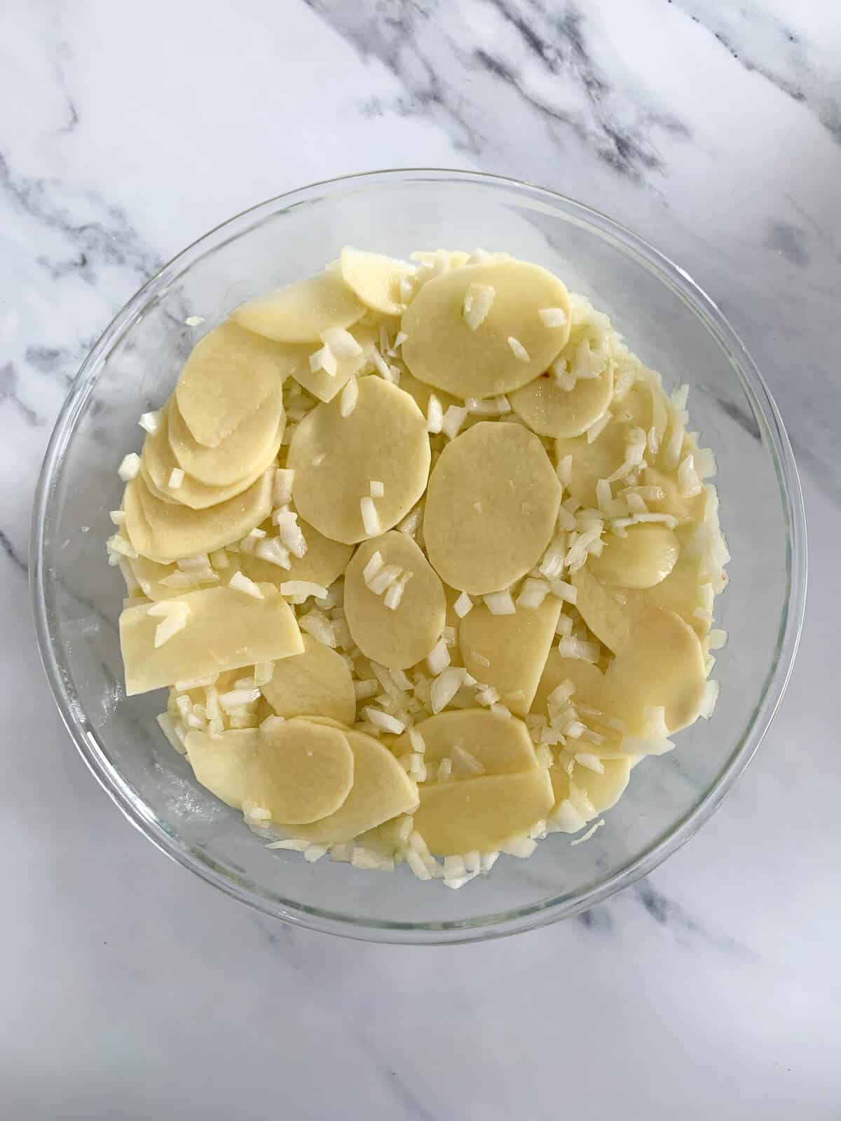 Potatoes mixed with onions and olive oil in a glass pyrex cake tin (before eggs are added) 