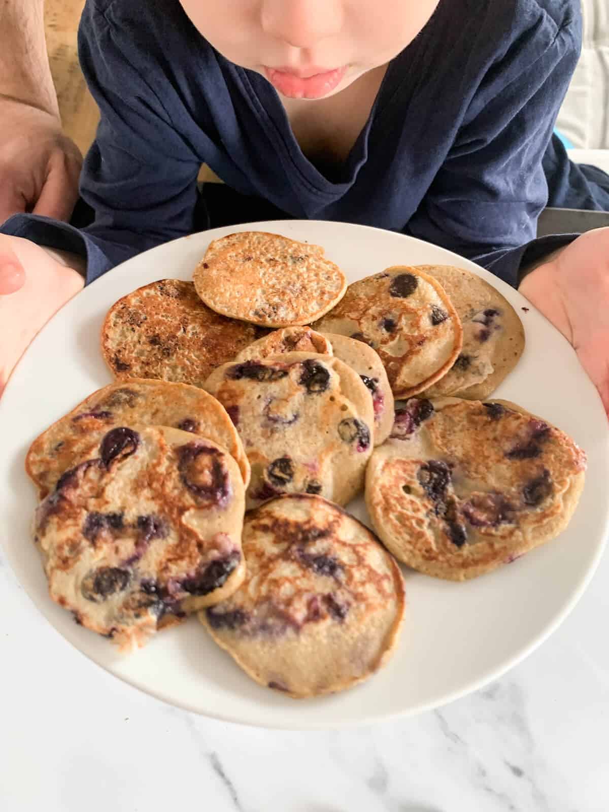 toddler holding a plate of pancakes 