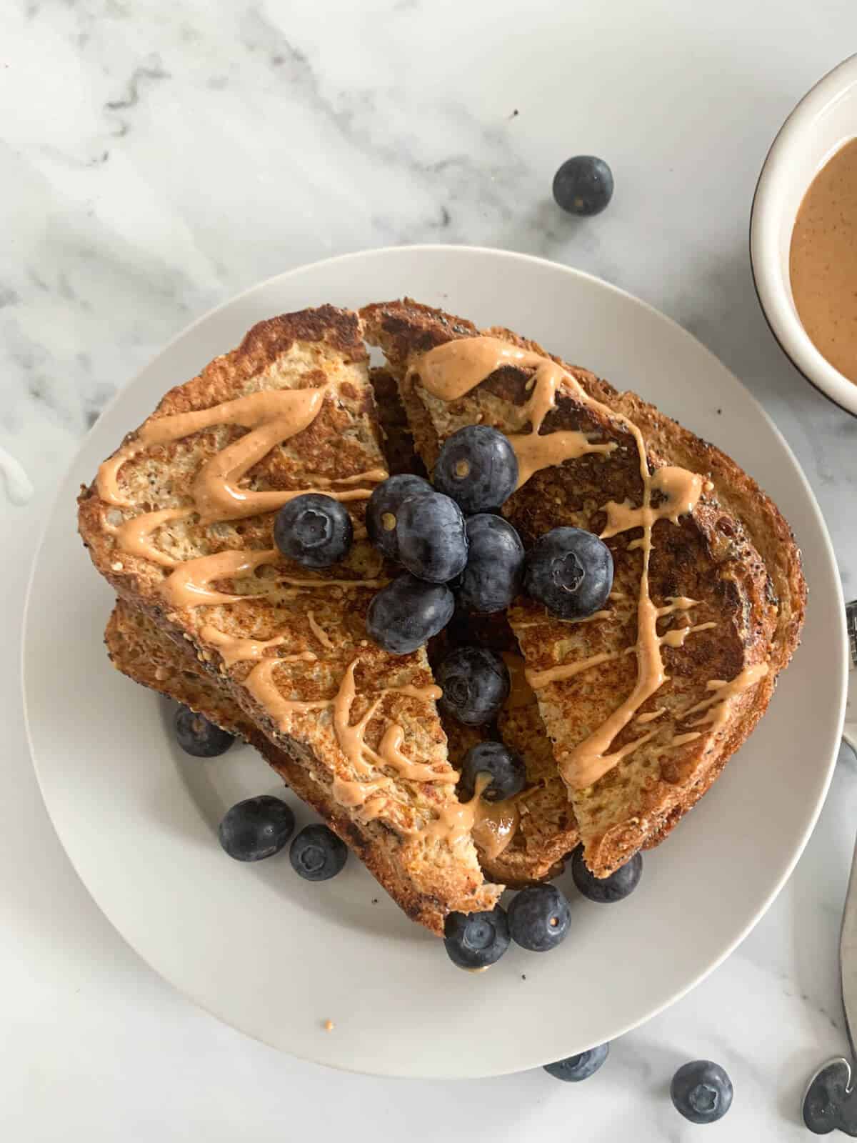 healthy french toast with blueberries with drizzled peanut butter on a white plate 