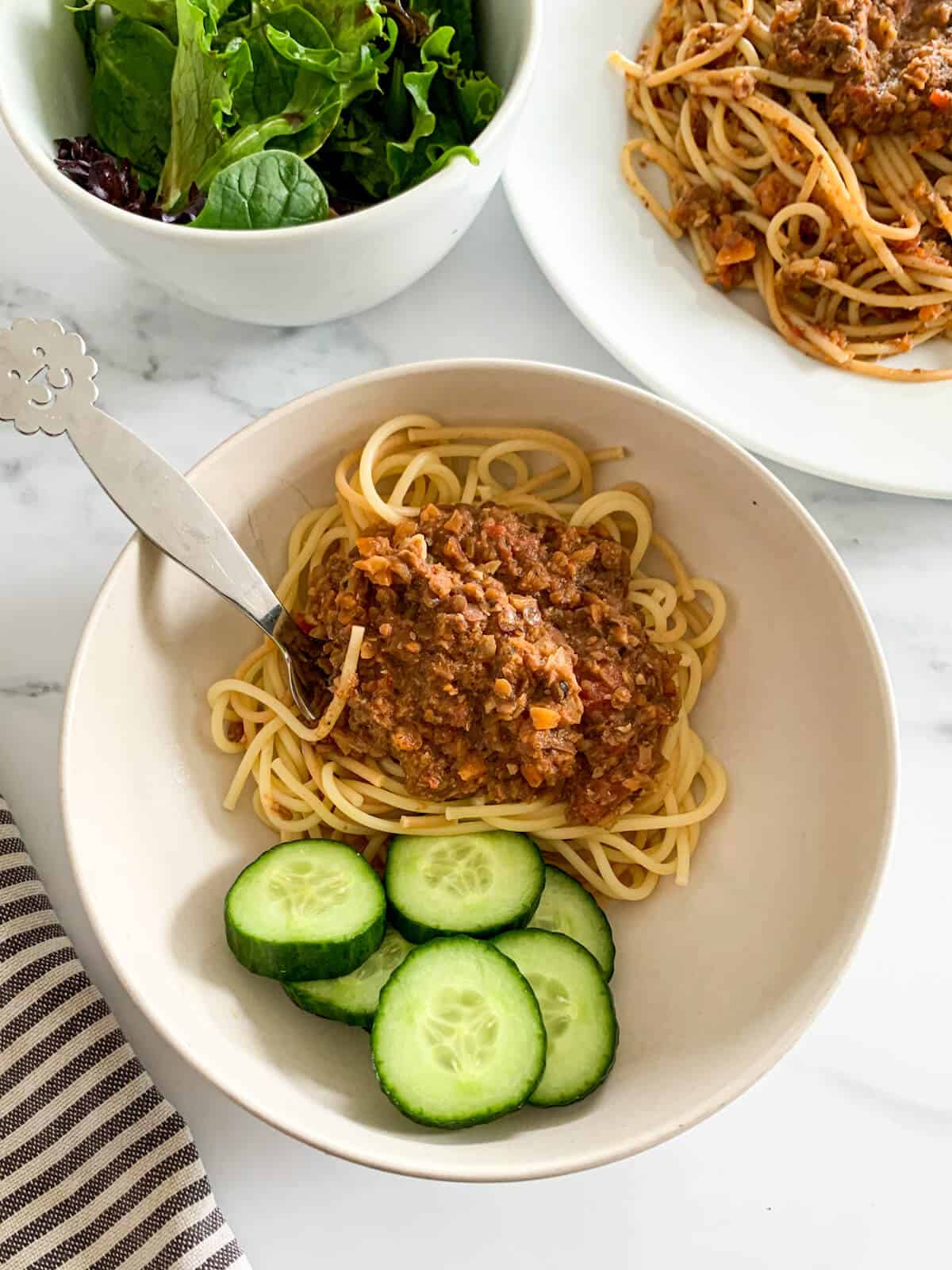plate of vegan spaghetti bolognese for toddler with a side of cut up cucumbers 