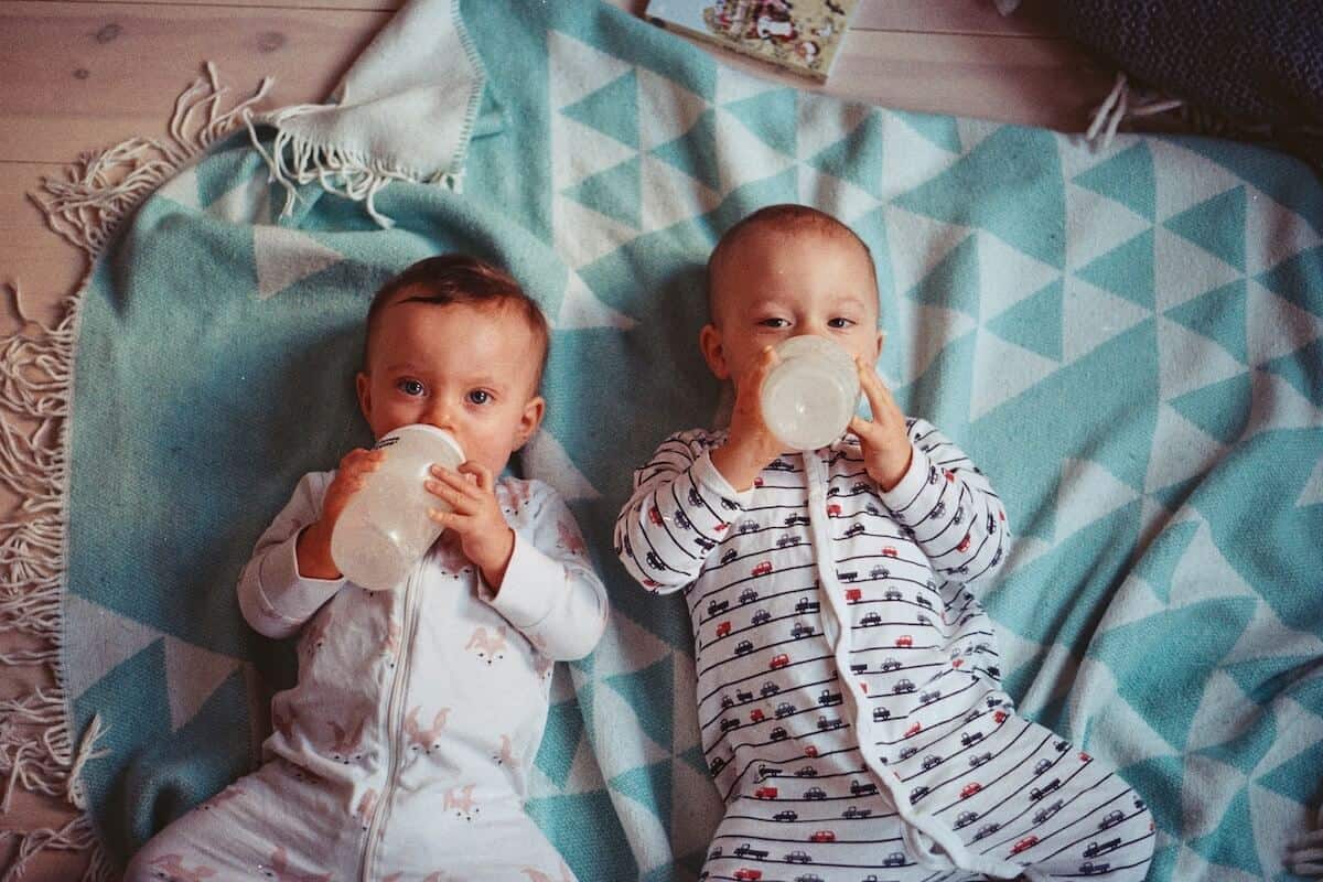 babies lying on a blanket drinking from a bottle 