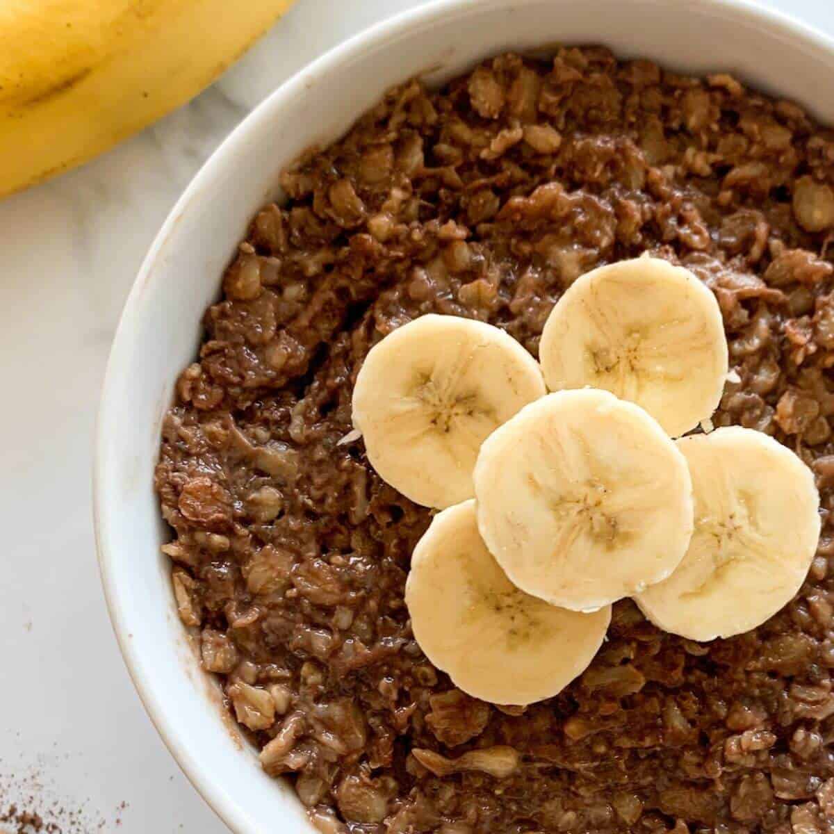 Healthy Chocolate Oatmeal with mashed banana in a white bowl topped with banana slices 