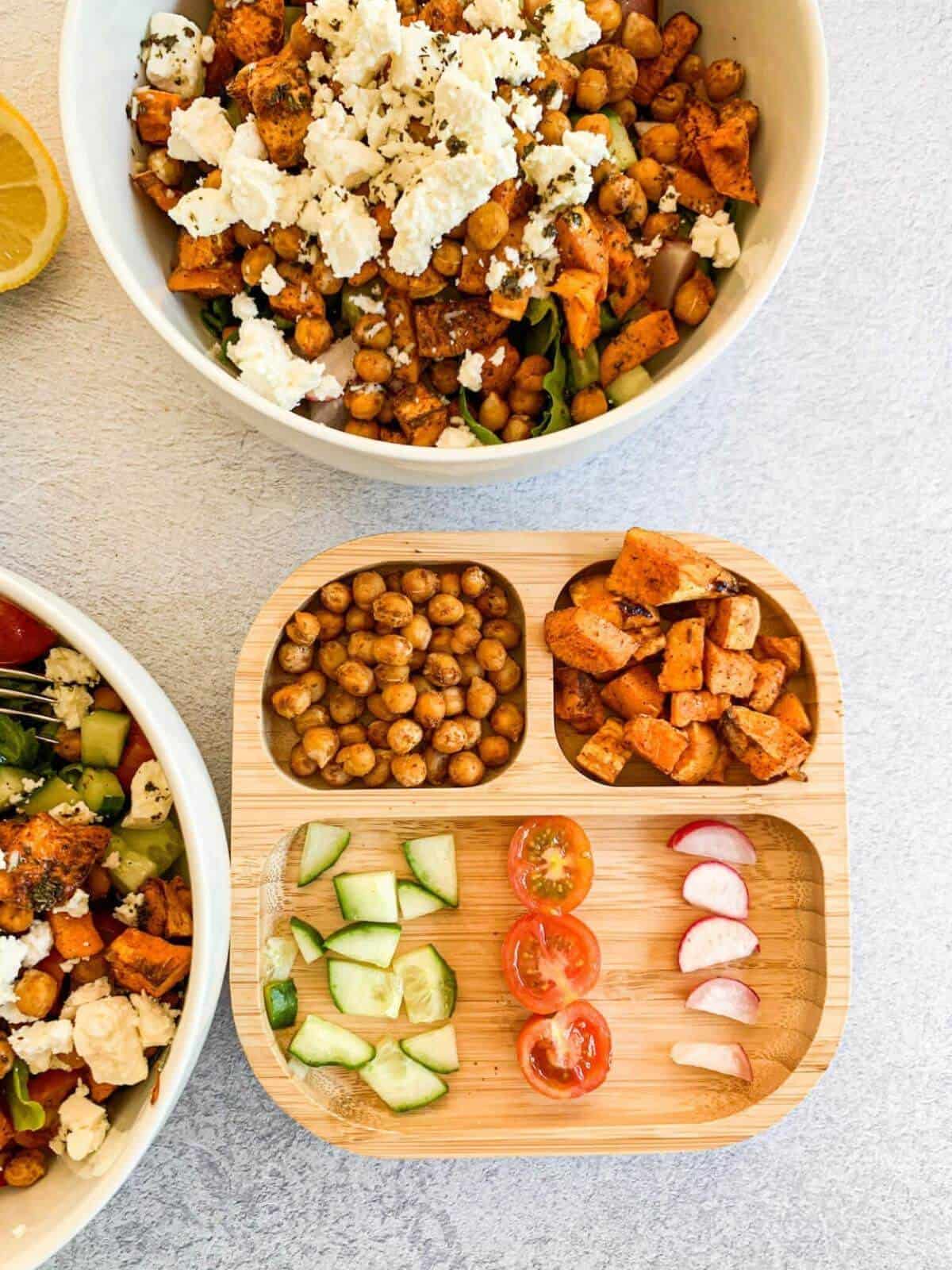 a bamboo plate for toddlers with roasted chickpeas, roasted sweet potato and chopped up cucumber, cherry tomatoes and radishes 