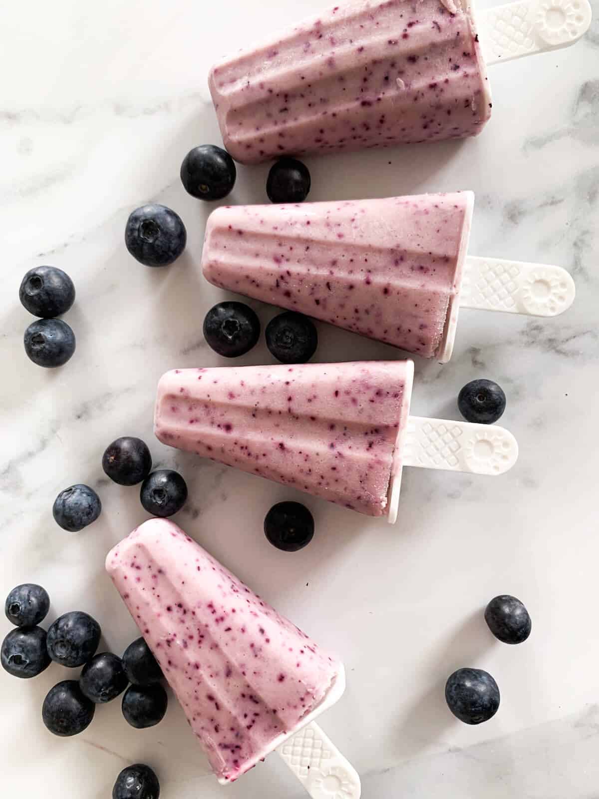 4 fruit popsicles surrounded by whole blueberries 