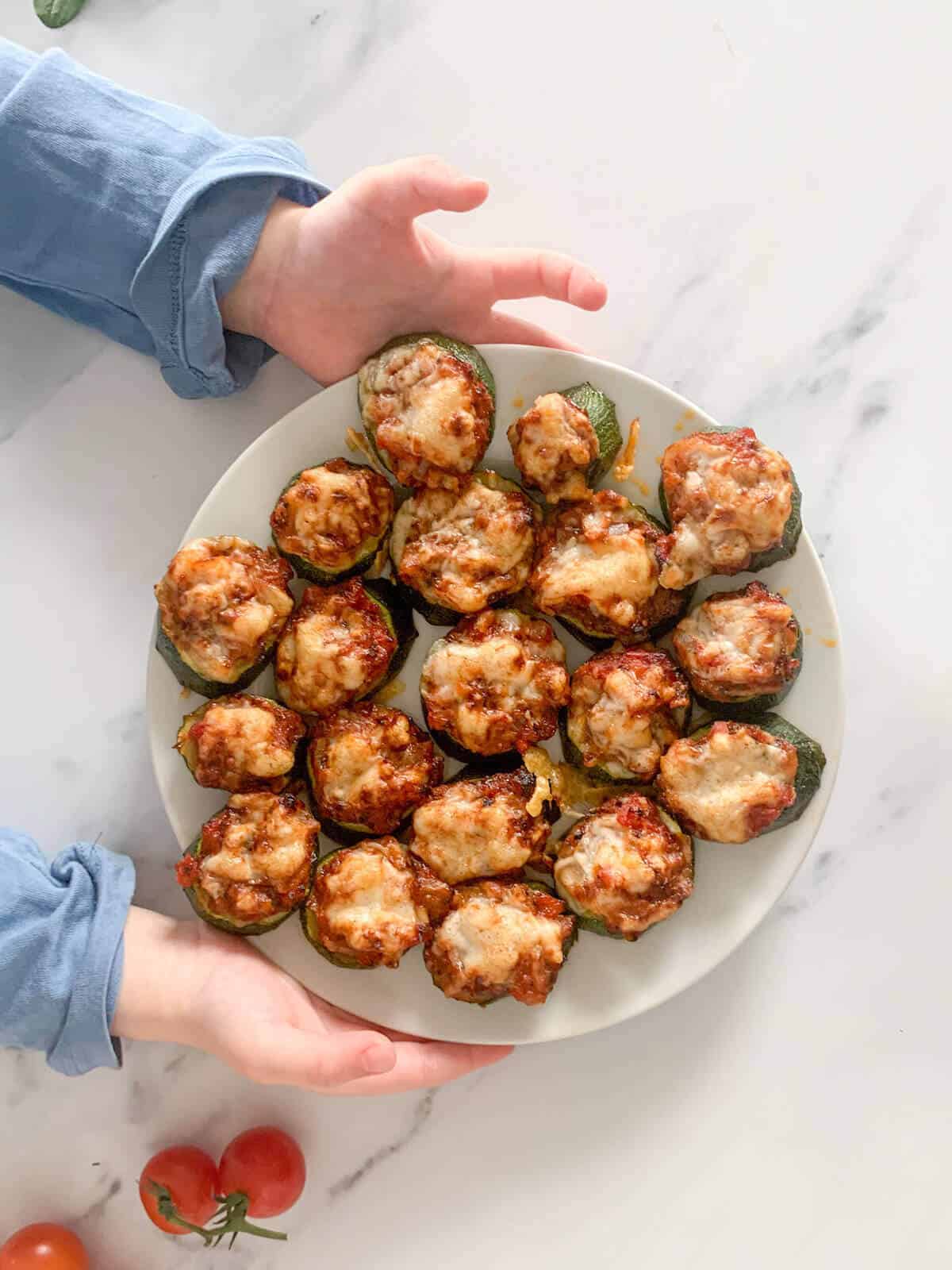 Mini Zucchini Pizza Bites on a plate held by a toddler 