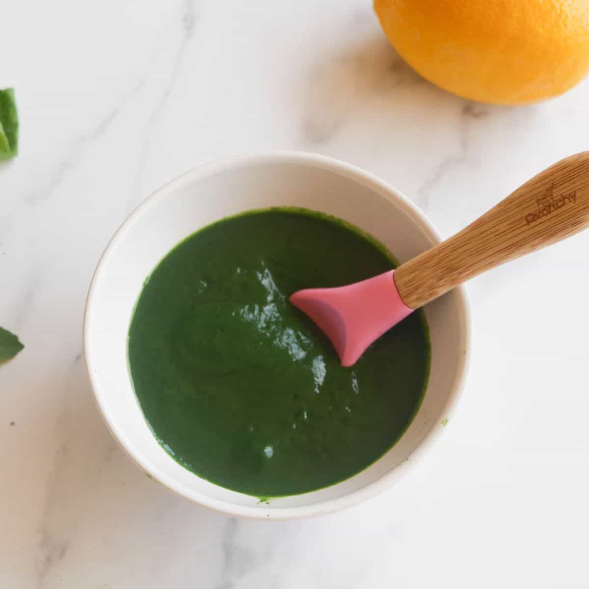 spinach puree in a white bowl with pink silicone spoon 