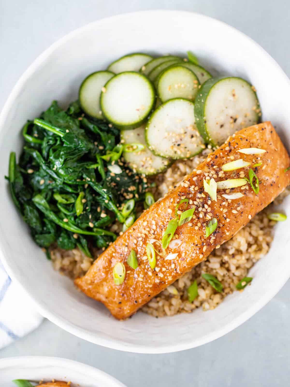 salmon filet in a brown rice bowl with spinach and pickled cucumbers