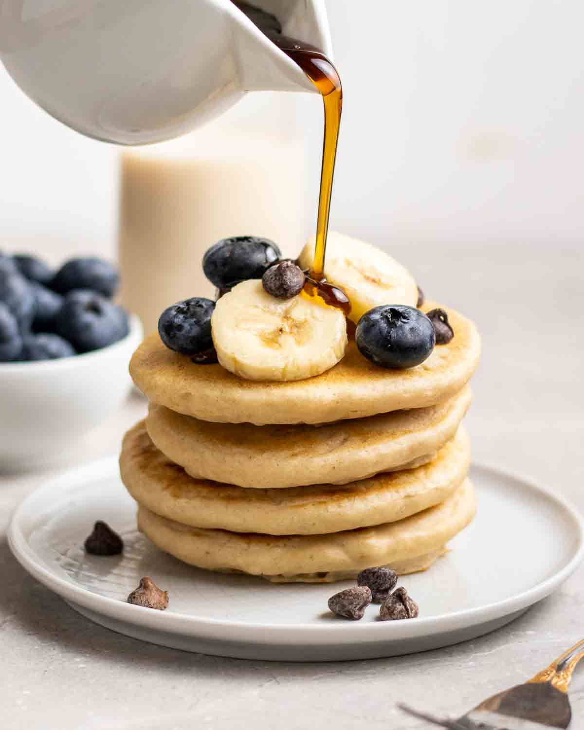 soy milk pancakes stacked with maple syrup being poured over 