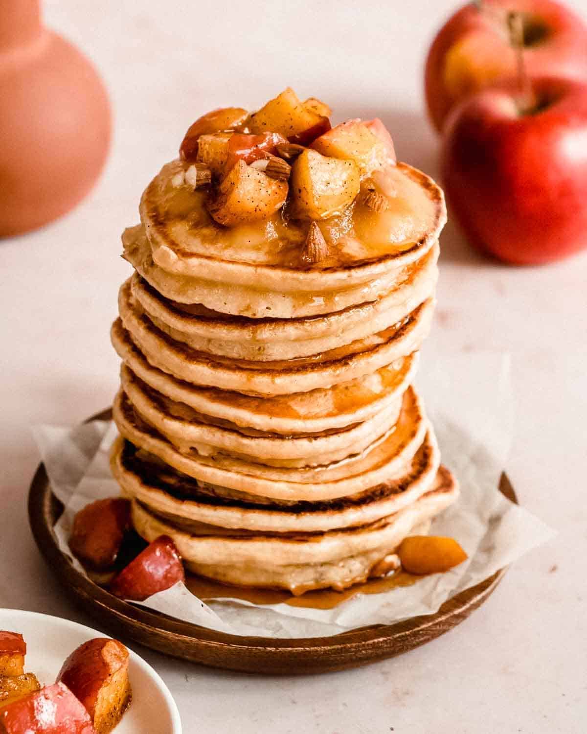 Stack of pancakes topped with chopped apples and some apples on the side.