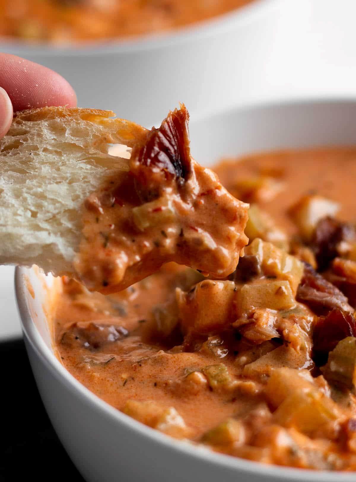 White bowl with smoked salmon chowder and slice of bread. 