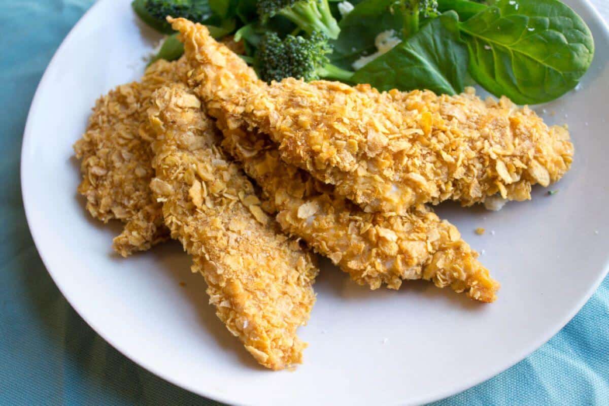 Chicken tenderloins on a white plate with salad and broccoli on the side. 