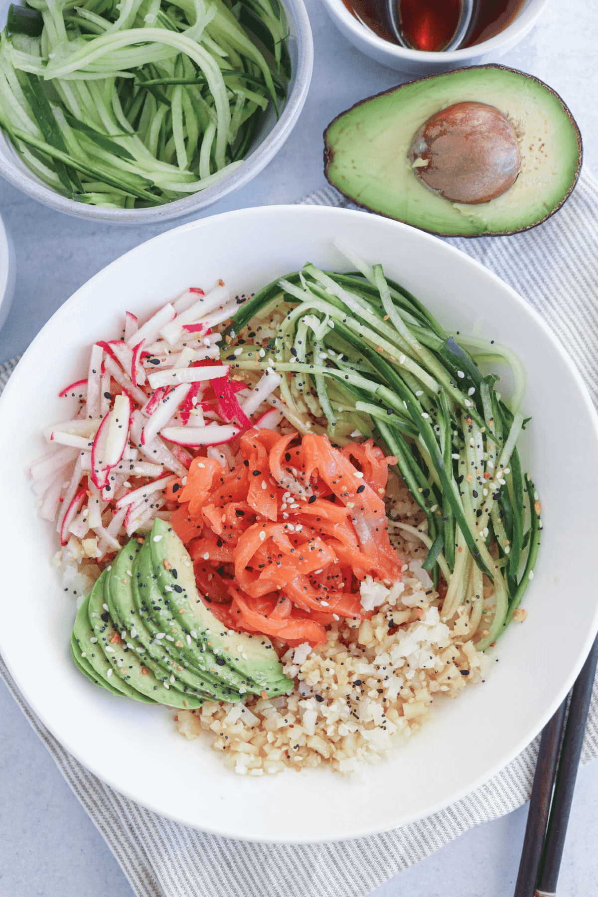 White plate with rice, shredded cucumbers, smoked salmon and avocadoes. 