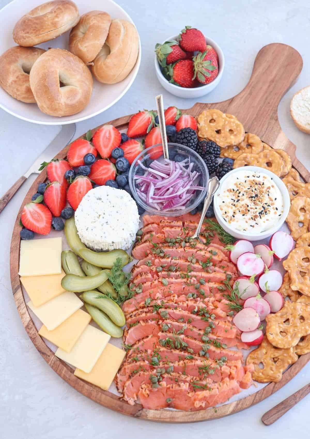 Wooden platter with crackers, smoked salmon, cheese, fruit and sour cucumbers. 