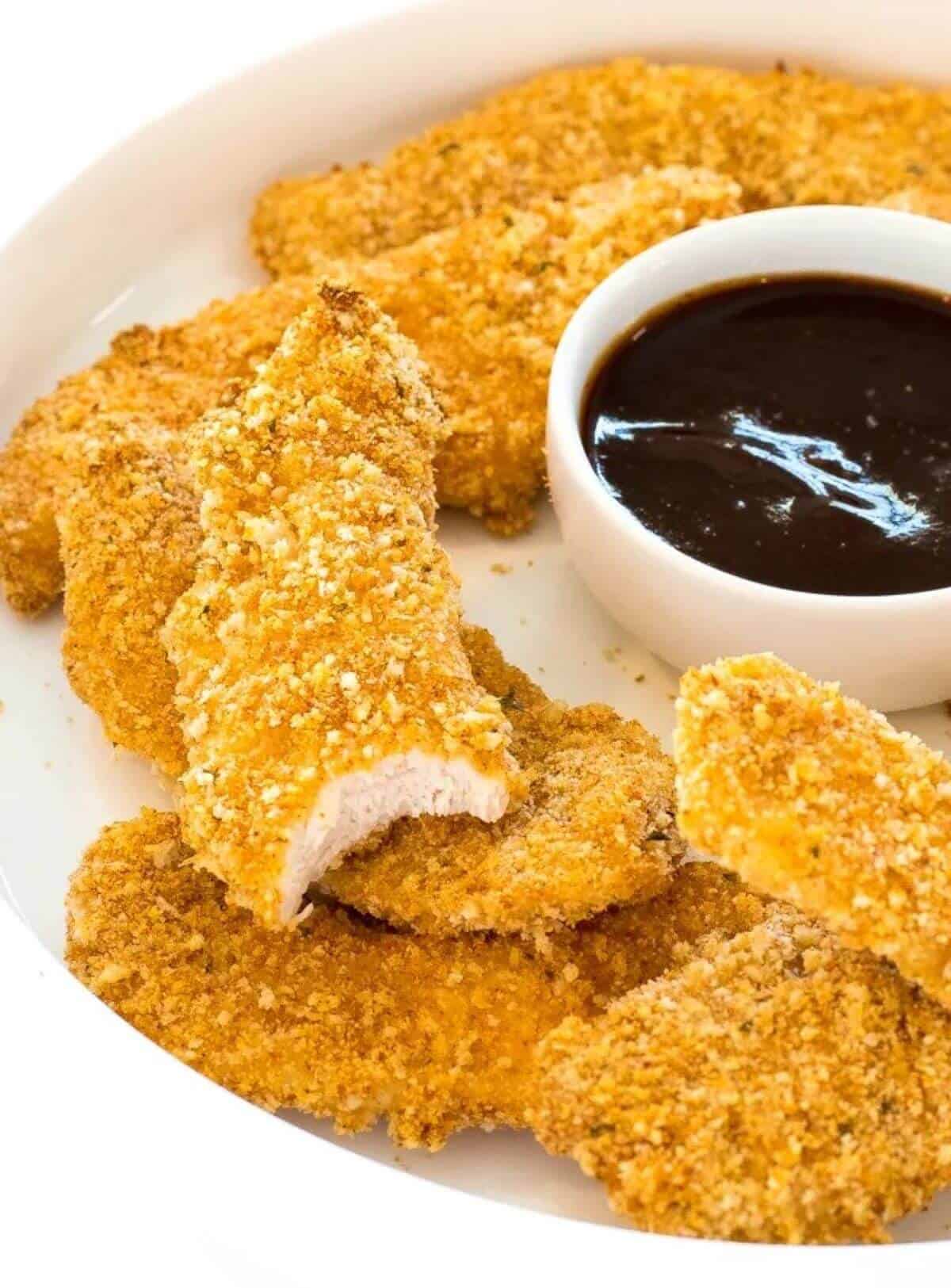 Baked chicken tenders on a white plate with sauce on the side. 