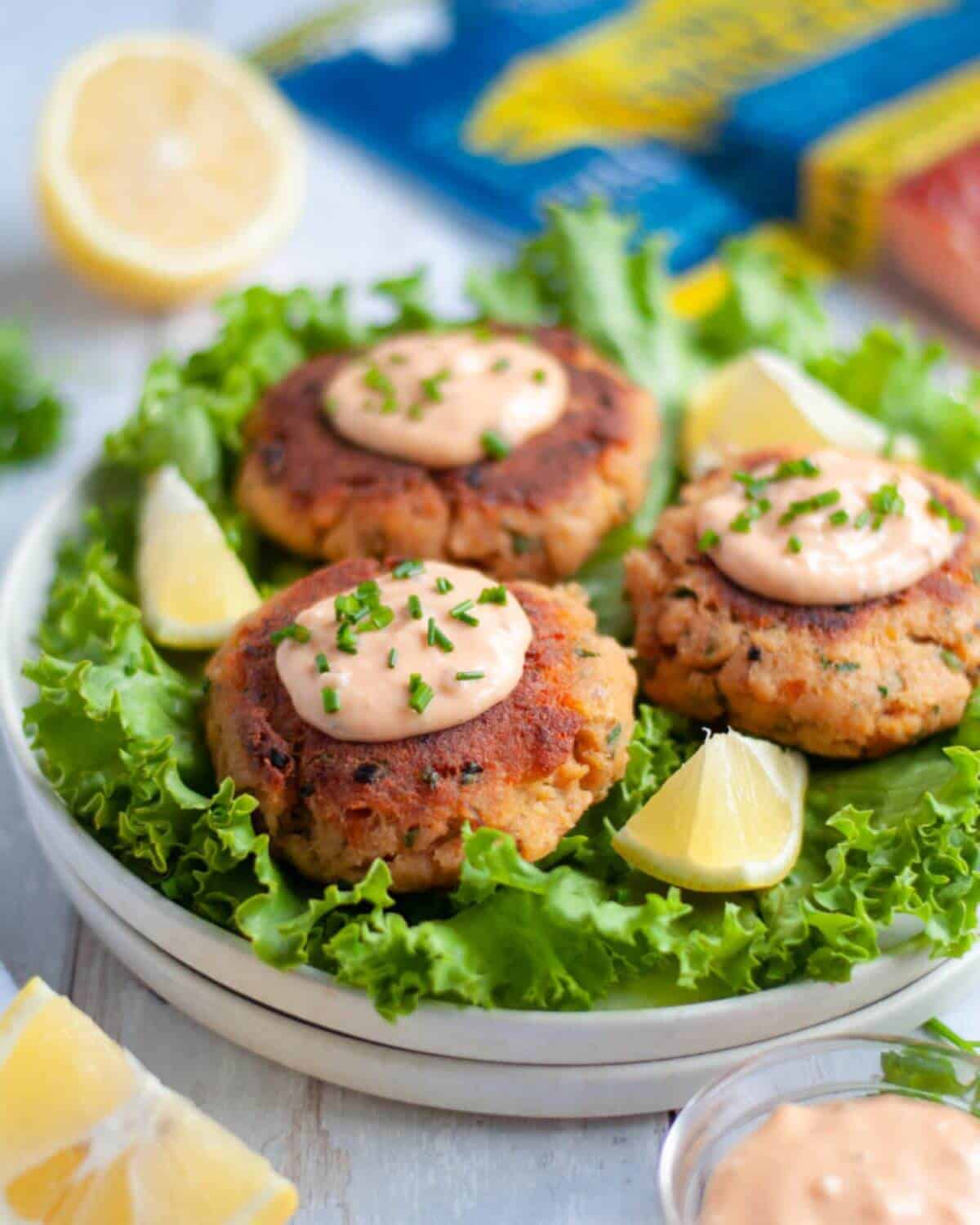 Three salmon cakes on top of rocket salad and garnished with cream sauce and herbs. 