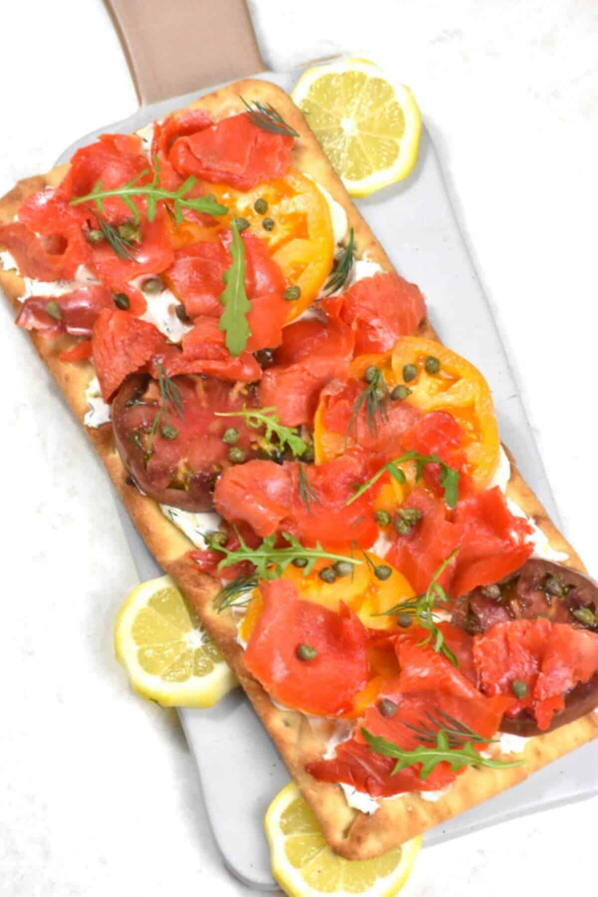 Flatbread with tomatoes, peppers and smoked salmon garnished with rocket salad and capers. 