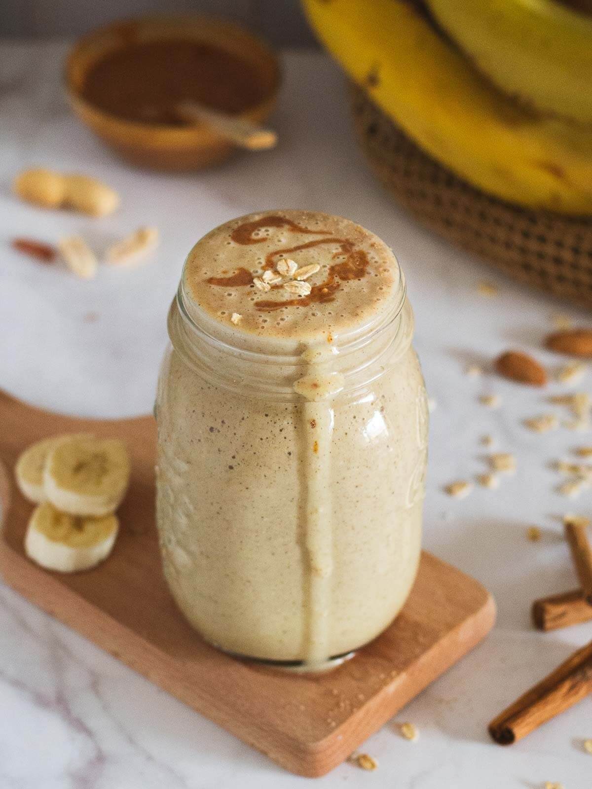 Jar with peanut butter oat milk smoothie and three banana slices on the side 