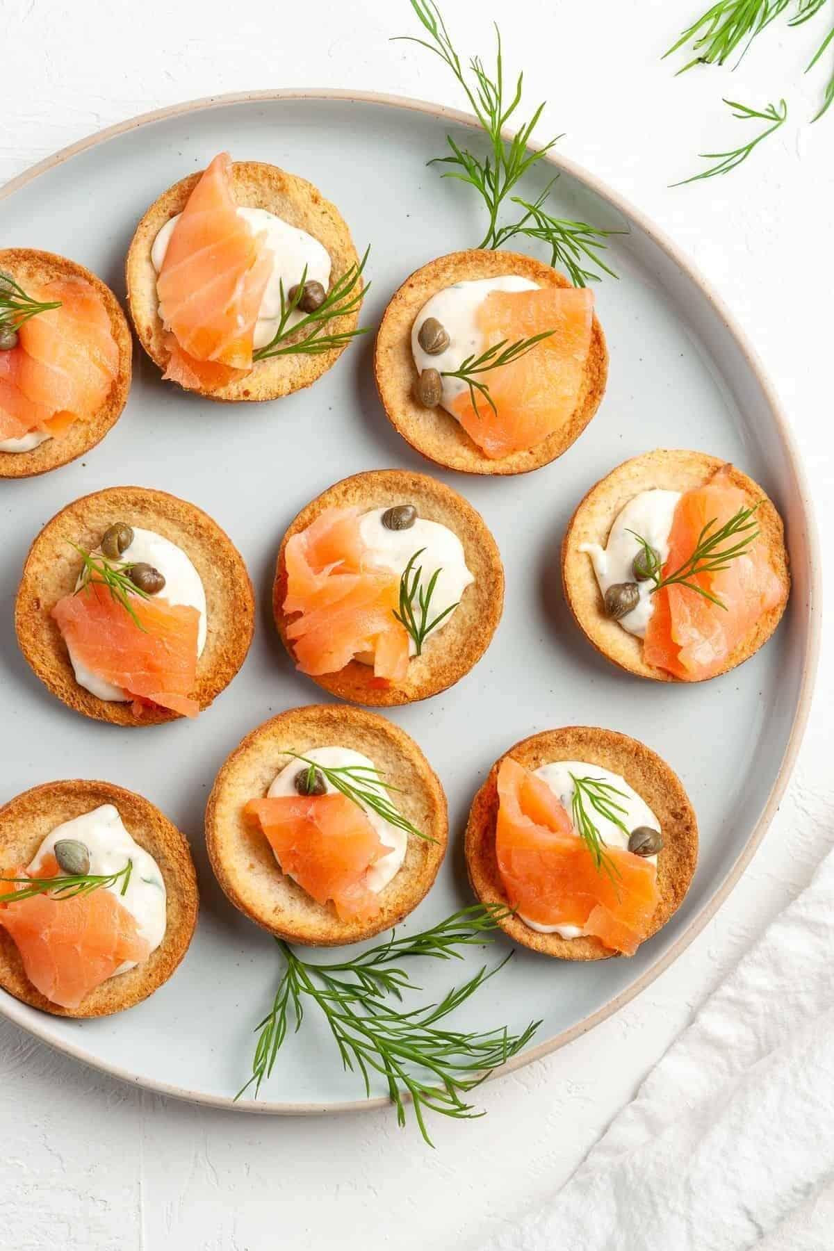 Plate with small canapes with cream and smoked salmon and garnished with herbs and capers. 