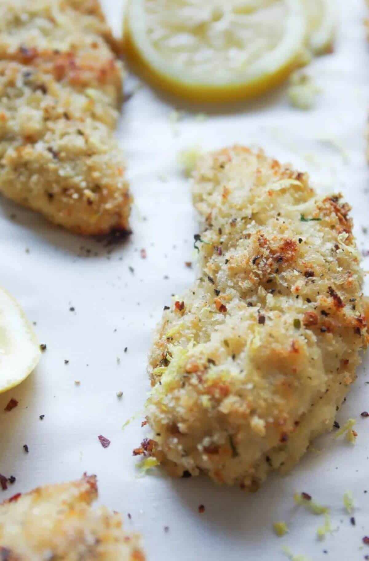 Two baked chicken tenders with a slice of lemon on the side.