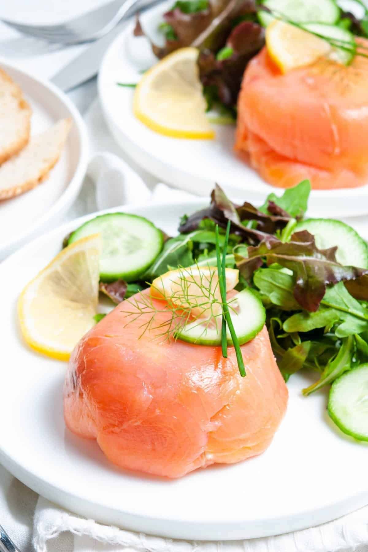 White plate with smoked salmon, rocket salad and garnished with cucumbers, lemons and herbs. 
