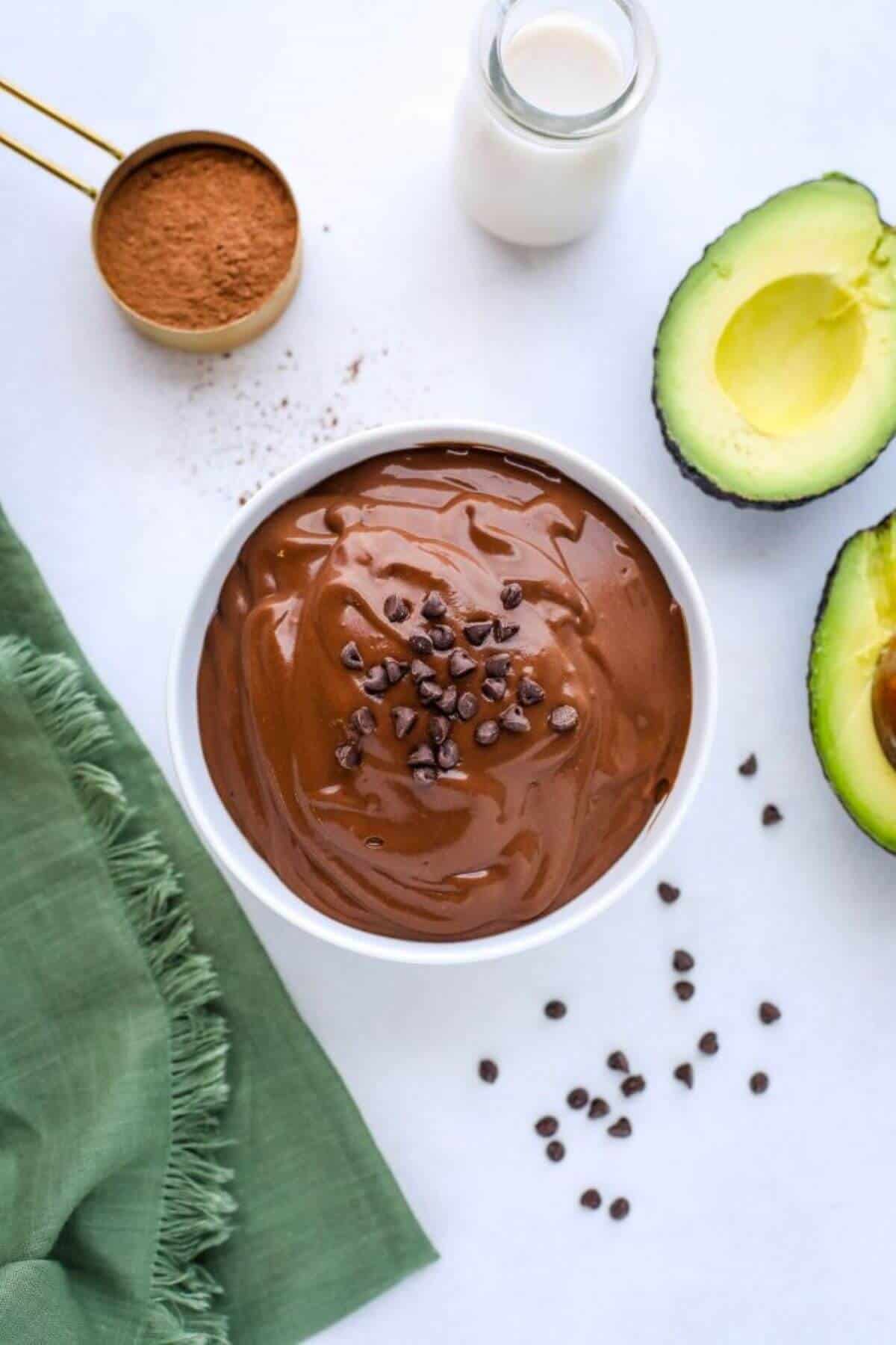 Jar with chocolate avocado smoothie. A spoon of cinnamon on the site, glass of milk and two halves of the avocado. 