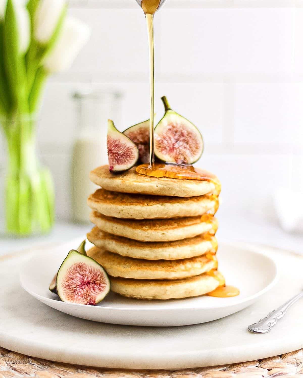 Stack of pancakes on a plate. Sliced fresh figs on the side and drizzled with syrup. 