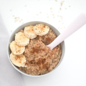 oatmeal for baby in a bowl with sliced bananas and a spoon dipped iin