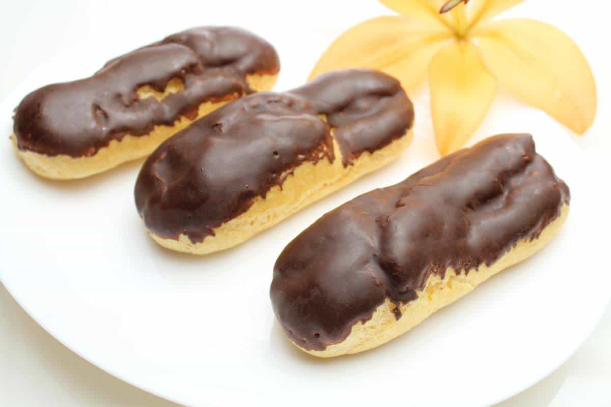 For foods that start with e, these 3 chocolate covered eclairs on a white plate are one of the most delicious