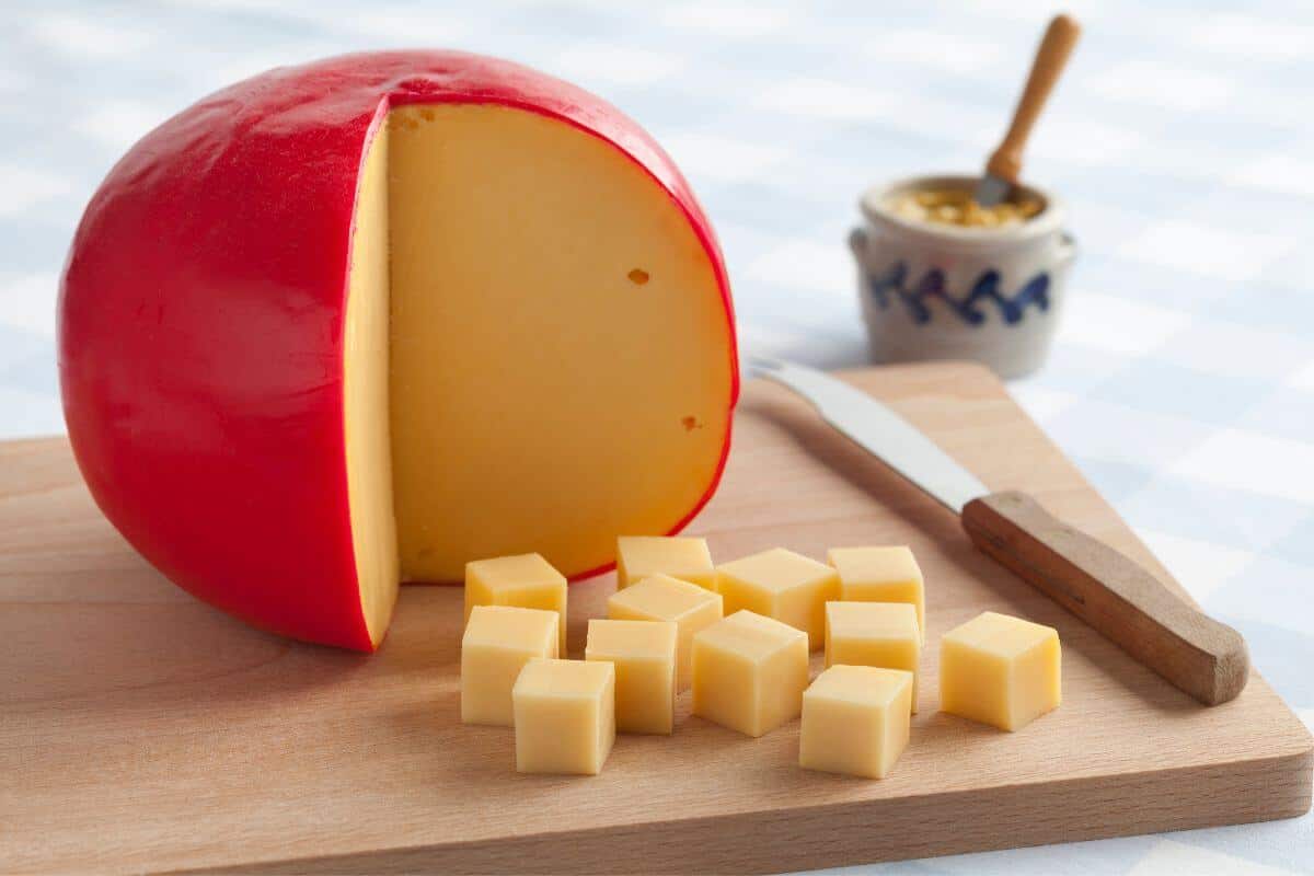 A large edam cheese on a cheeseboard, with a quarter cut out and cut into small cubes on the board