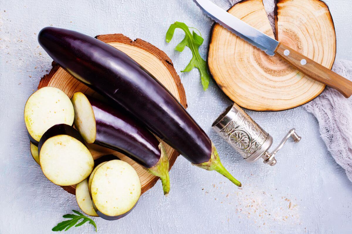 2 eggplants, one whole, one sliced, sitting on a wooden board