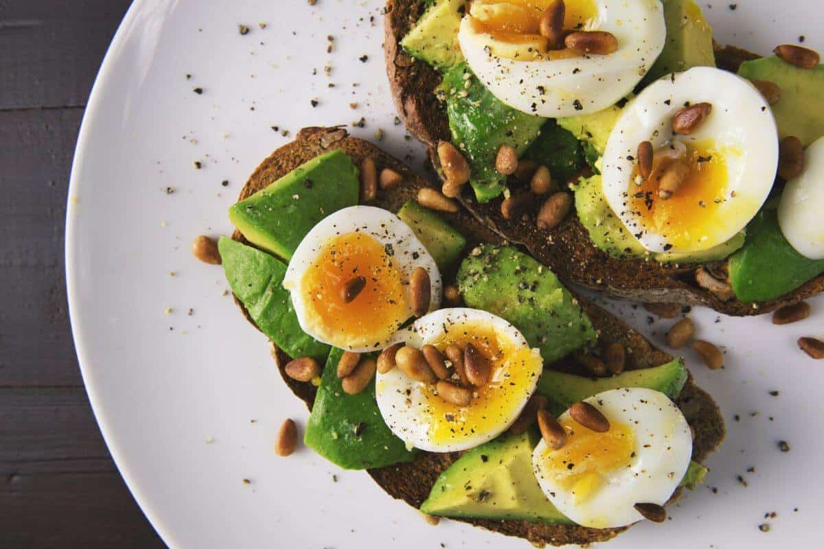 Soft boiled eggs, cut in half, on avocado toast with some roasted pine nuts and sprinkled with black pepper