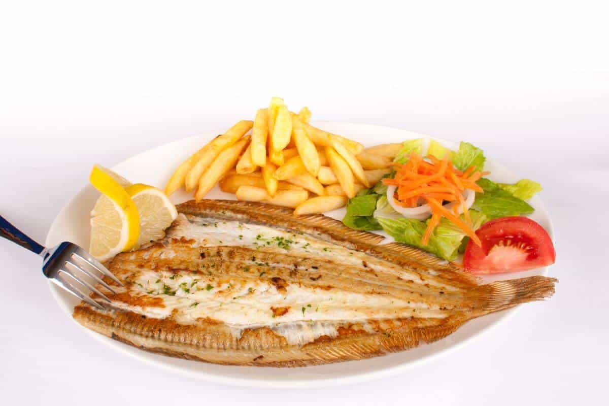Pan-fried english sole on a plate with a slice of lemon, fries, and salad