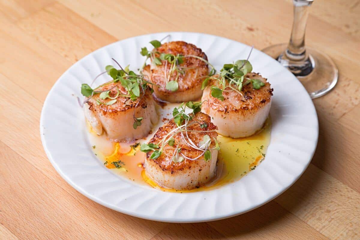 4 seared scallops on a white plate, topped with greens