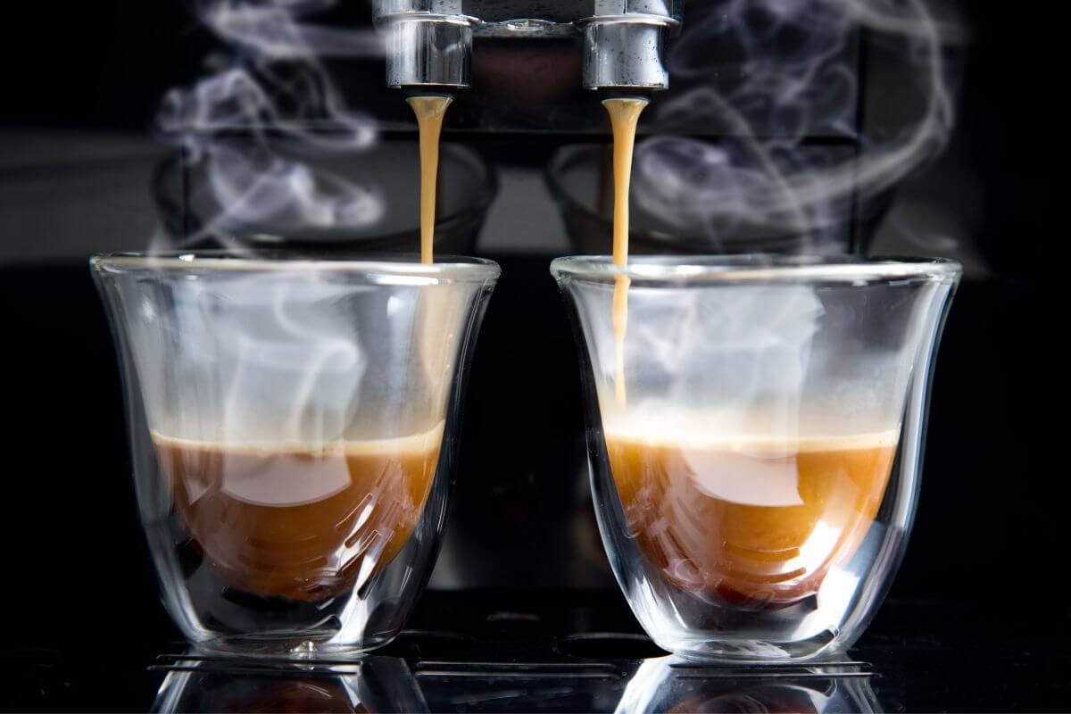 2 glass coffee cups with espresso pouring into them and steam rising up 