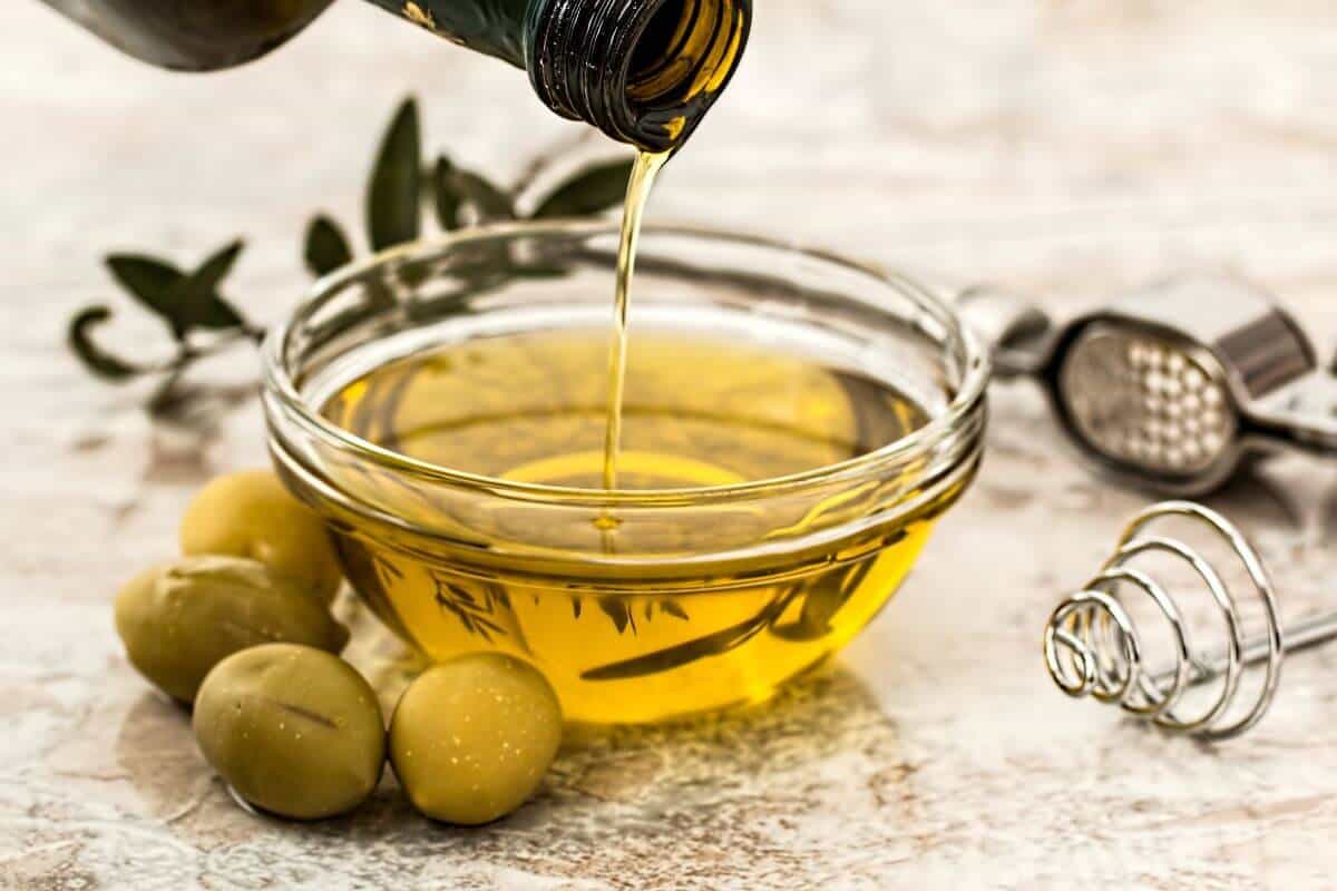 Extra virgin olive oil being poured into a small bowl, with olive on the table next to the bowl