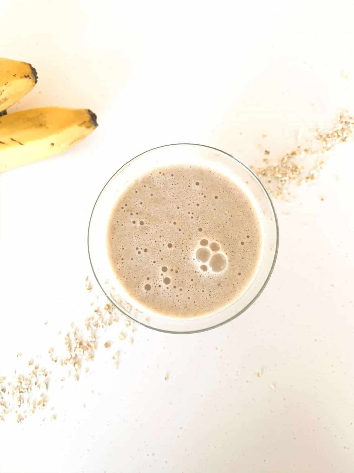 Glass with a beige-colored smoothie and 2 bananas on the side