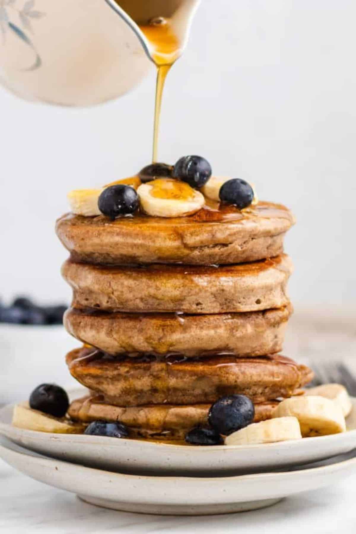 Stack of thick pancakes on a plate. Blueberries and sliced bananas on the side. 