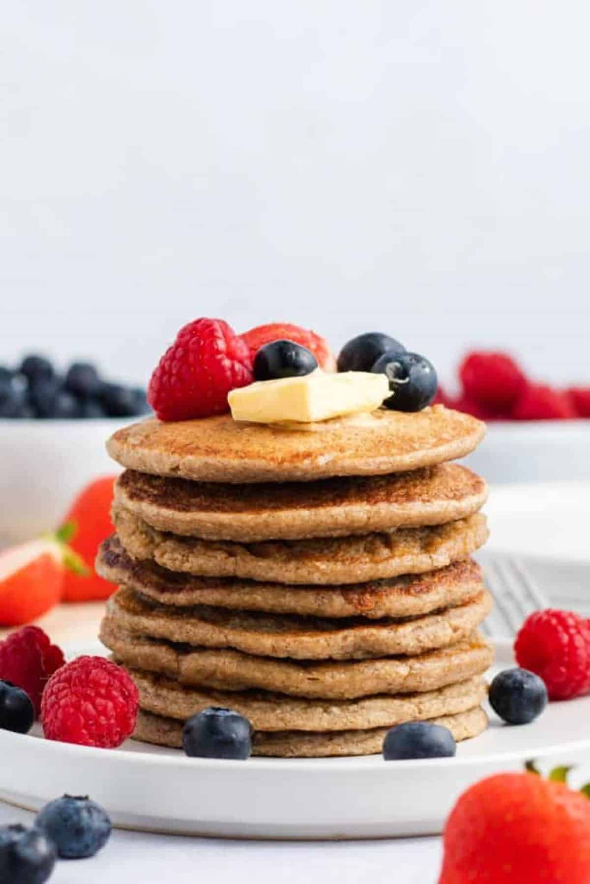 Stack of pancakes on a plate with blueberries and raspberries on the side. 